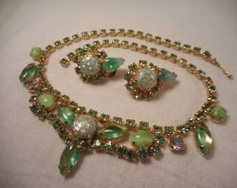 May include: A vintage jewelry set featuring a necklace and matching earrings. The set has a gold-tone metal setting with green and clear rhinestones. The necklace has a bib design with various shapes of green stones.