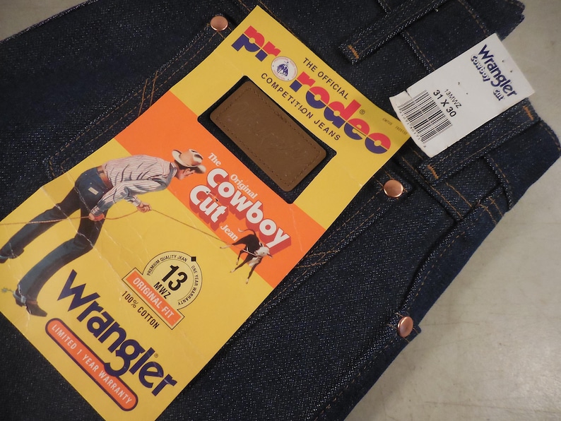 May include: A pair of blue denim jeans with a Wrangler label and a Rodeo competition jeans tag. The tag features a cowboy riding a horse and the text "The Original Cowboy Cut Jeans".