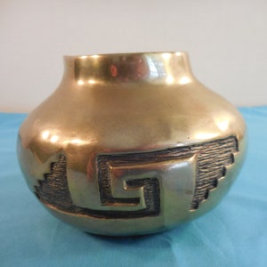 May include: A gold-colored ceramic vase with a geometric design. The vase has a round body and a wide opening.