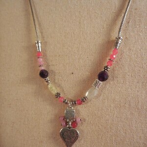 May include: A silver necklace with a heart pendant and colorful beads. The pendant has a heart shape with an ornate design and the words "Listen to Your Heart". The beads are pink, purple, and white.
