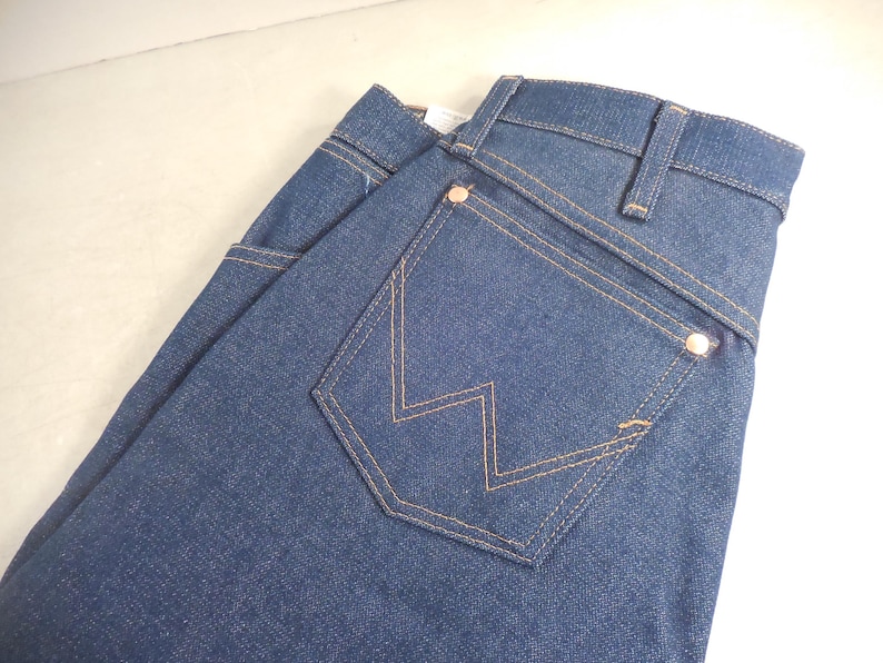 May include: A pair of dark blue denim jeans with a back pocket featuring a distinctive W-shaped stitching.