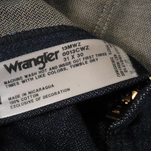 May include: A white Wrangler jeans care label with black text. The label says "Machine wash hot and inside out first three times with like colors, tumble dry. Made in Nicaragua, 100% cotton, exclusive of decoration. 13MWZ 0013Cwz 31 x 30."