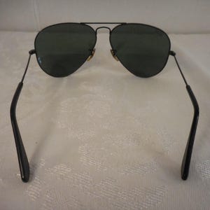 May include: Black aviator sunglasses with dark green lenses. The sunglasses have a thin, black metal frame and temples. The lenses are teardrop-shaped. The bridge and hinges are gold-colored. A classic style for eye protection.