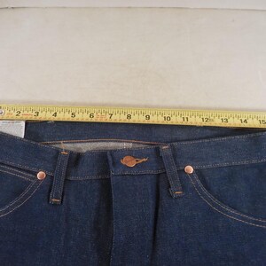 May include: A pair of dark blue denim jeans with a copper-colored button and rivets. The jeans have a standard five-pocket design and a straight leg.