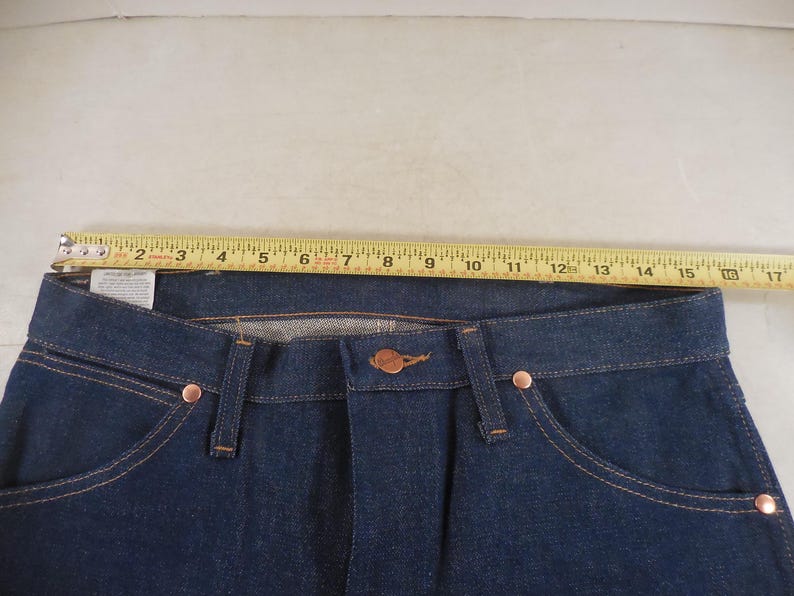May include: A pair of dark blue denim jeans with a copper-colored button and rivets. The jeans have a standard five-pocket design and a straight leg.