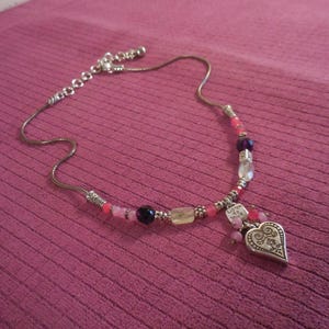 May include: Silver-toned necklace with a heart pendant and colorful beads. The pendant has an ornate design and the necklace features pink, purple, and clear beads. The text "Listen to your heart" is on a small charm.