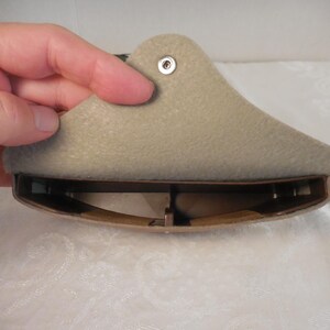 May include: A beige shoe stretcher, held by a hand, with a curved, padded top and a brown, adjustable base. The stretcher has a metal rivet and is designed to expand the shoe's width and length.
