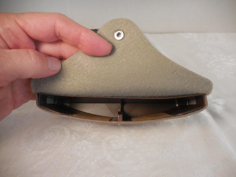 May include: A beige shoe stretcher, held by a hand, with a curved, padded top and a brown, adjustable base. The stretcher has a metal rivet and is designed to expand the shoe's width and length.