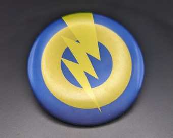 May include: A blue and gold round button with a yellow lightning bolt design.