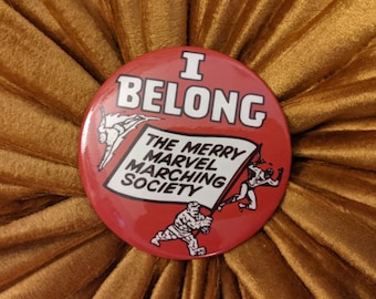 May include: Red button with white text that reads "I Belong The Merry Marvel Marching Society". The button features a comic book style illustration of three superheroes.