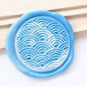 Puede incluir: Un sello de cera azul con un diseño de olas superpuestas en blanco y azul.