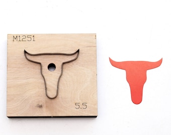 May include: A wooden die-cut tool with a metal outline of a bull's head, next to a cut-out bull's head in red. The tool is marked with "M1251" and "5.5". The bull head is approximately 5.5 inches wide.