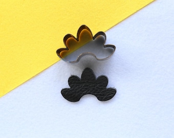 May include: Two metal cookie cutters in the shape of a flower. The top cutter is silver and the bottom cutter is black.