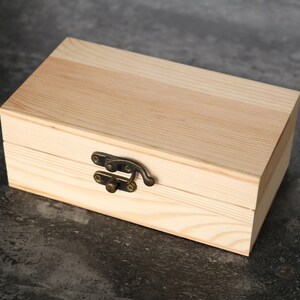 May include: A wooden box with a hinged lid and a brass latch. The box is made of light-colored wood and has a natural finish.