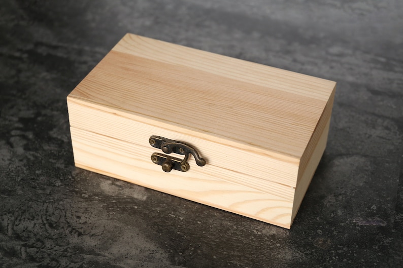May include: A wooden box with a hinged lid and a brass latch. The box is made of light-colored wood and has a natural finish.