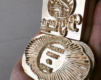 May include: Two brass stamps, one with a sun and house design and the text "Big Barn Creations", the other with a sunburst design and the text "House of Llama Wonder"