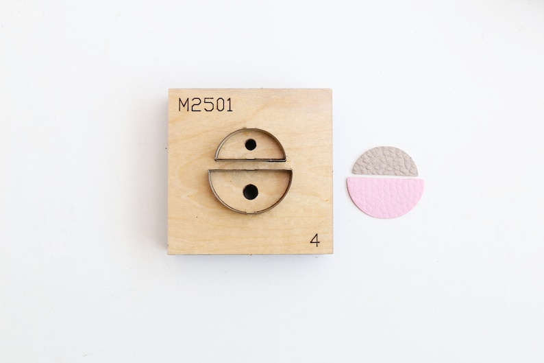 May include: A wooden punch tool with the number "M2501" and the number "4" printed on it. The punch tool has a metal die cut out in the shape of two half circles with a small hole in the center of each half circle. A sample of the die cut shape is shown next to the punch tool, made of two pieces of leather in pink and gray.