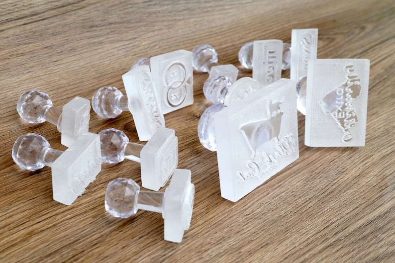 May include: A collection of clear plastic stamps with various designs, including a heart, a goat, and a ring. The stamps are on a wooden surface.