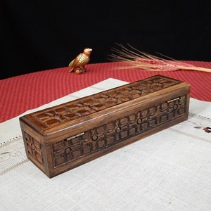 May include: A wooden box with a hinged lid, intricately carved with a geometric pattern. The box is made of dark brown wood and has a natural finish.