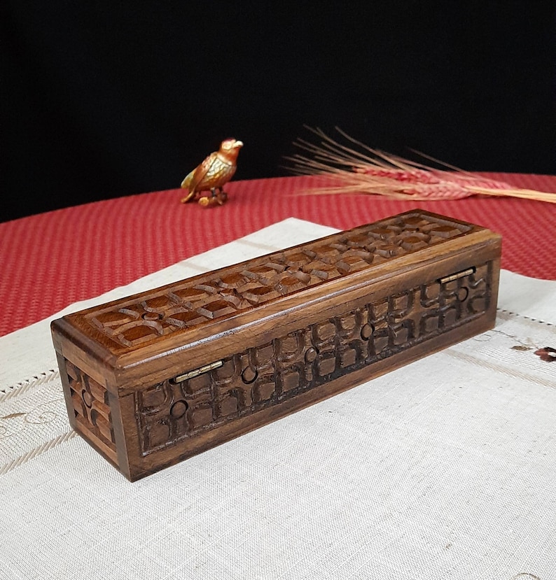 May include: A wooden box with a hinged lid, intricately carved with a geometric pattern. The box is made of dark brown wood and has a natural finish.