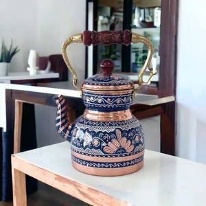 May include: A copper teapot with a blue and white floral design. The teapot has a wooden handle and a brass spout.
