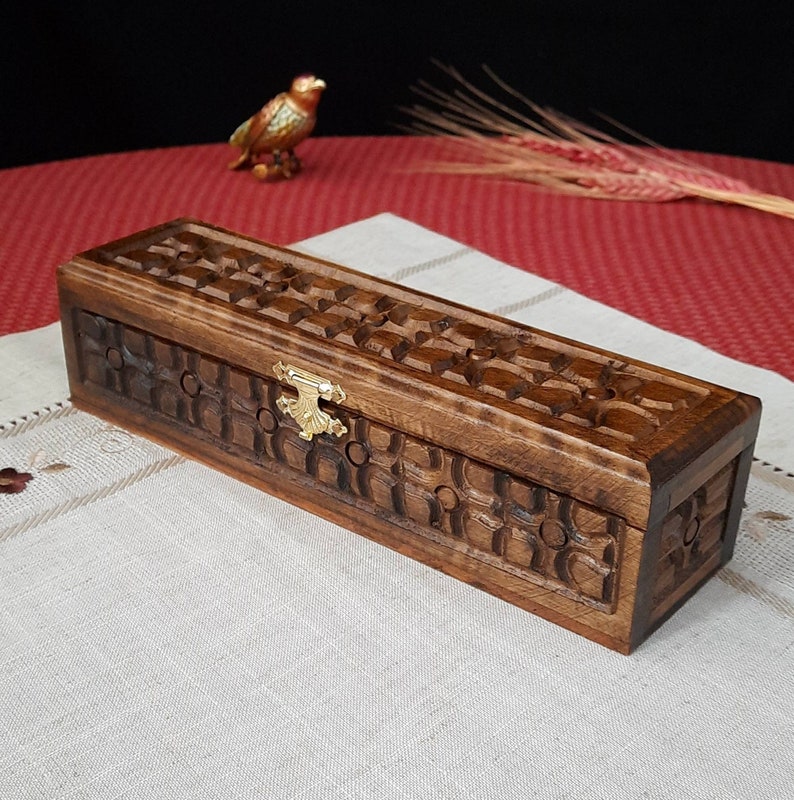 May include: A wooden box with a carved design and a brass latch. The box is brown and has a rectangular shape.
