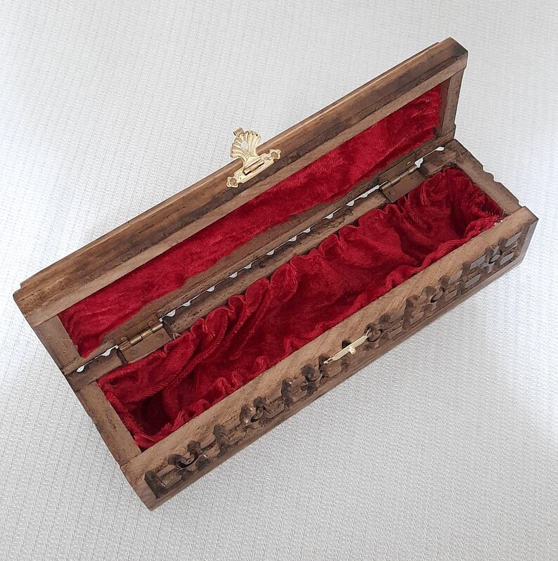 May include: A wooden box with a red velvet interior. The box has a carved design and a brass latch.