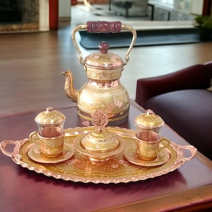 May include: A copper and brass Turkish tea set with a teapot, two cups, a sugar bowl, and a tray. The set features intricate floral designs and a gold finish.