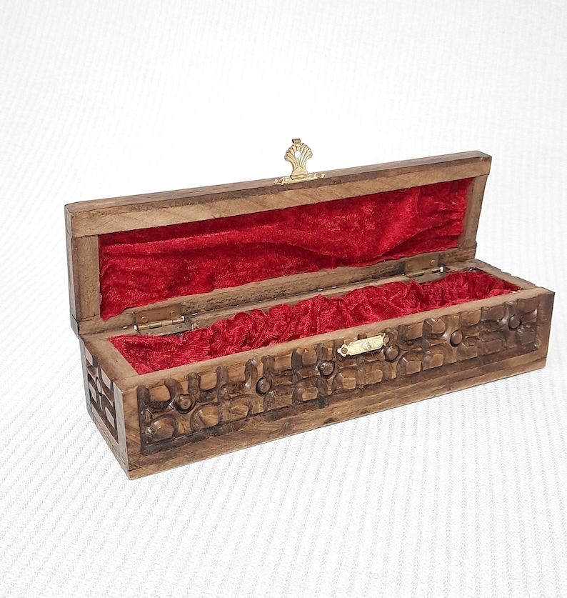 May include: A wooden box with a carved design and a red velvet interior. The box has a brass latch and hinges.