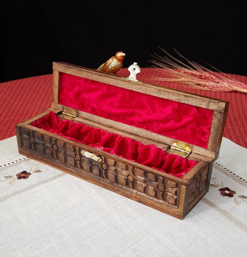 May include: A wooden box with intricate carvings and a red velvet interior. The box is open and has a small bird figurine on top of the lid.