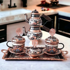 May include: A traditional Turkish coffee set with a copper tray, two cups, a sugar bowl, and a three-tiered teapot. The set is decorated with intricate hand-painted floral designs in black, white, and red.