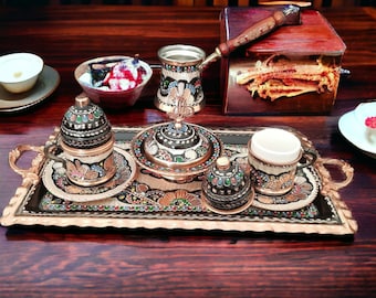 May include: A set of Turkish coffee cups and a pot with intricate hand-painted designs in black, gold, and red on a wooden tray. The cups and pot are made of copper and have a traditional design.