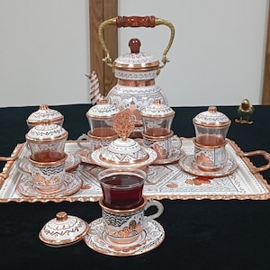 May include: A white and copper Turkish tea set with a teapot, six cups, and a tray. The cups and teapot have intricate floral designs.
