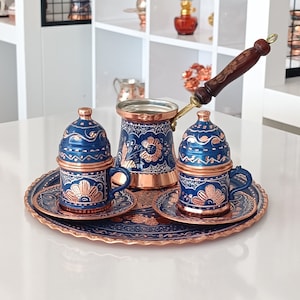 Könnte beinhalten: Ein traditionelles türkisches Kaffeekännchen-Set mit einer Kupferkanne und zwei Tassen mit blauen und goldenen Blumenmustern. Das Set befindet sich auf einem Kupfertablett mit einem blauen und goldenen Blumenmuster.