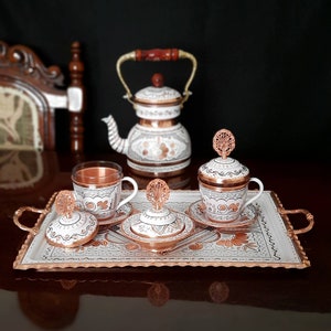 May include: A white and copper Turkish coffee set with a teapot, two cups, and a tray. The set features intricate floral designs and is perfect for serving traditional Turkish coffee.