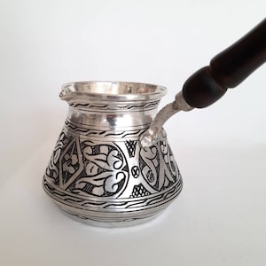 May include: A silver Turkish coffee pot with a black wooden handle and intricate floral designs.