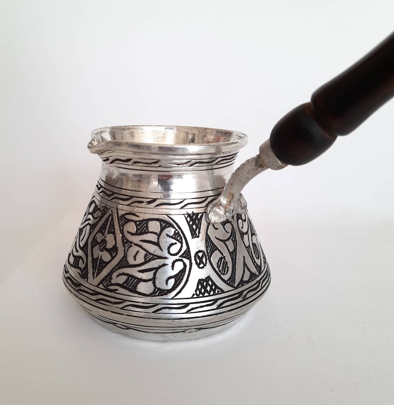 May include: A silver Turkish coffee pot with a black wooden handle and intricate floral designs.