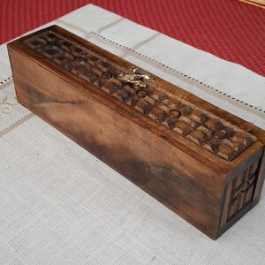 May include: A wooden incense holder with intricate carvings and a gold metal accent. The holder is rectangular and has a dark brown finish.