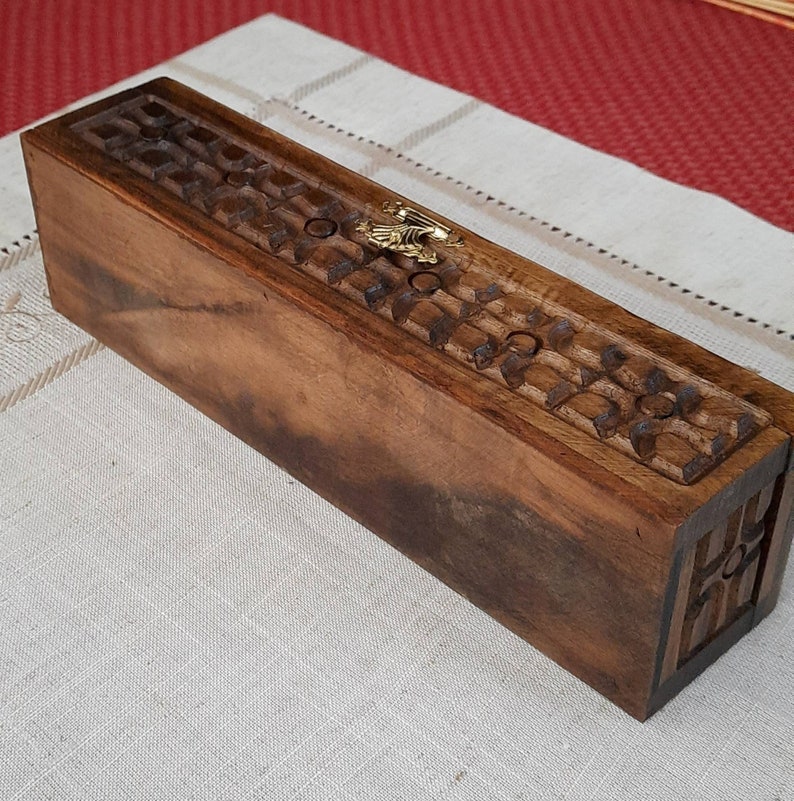 May include: A wooden incense holder with intricate carvings and a gold metal accent. The holder is rectangular and has a dark brown finish.