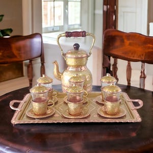 May include: A traditional Turkish tea set with a copper teapot and six small glasses with lids. The set is arranged on a copper tray with intricate designs.