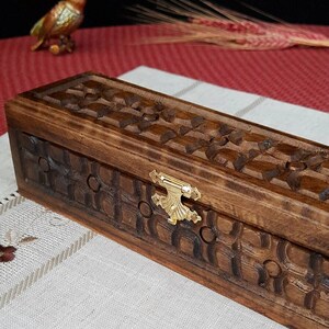 May include: A rectangular wooden box with a carved design and a gold metal latch. The box is made of dark wood and has a natural finish.