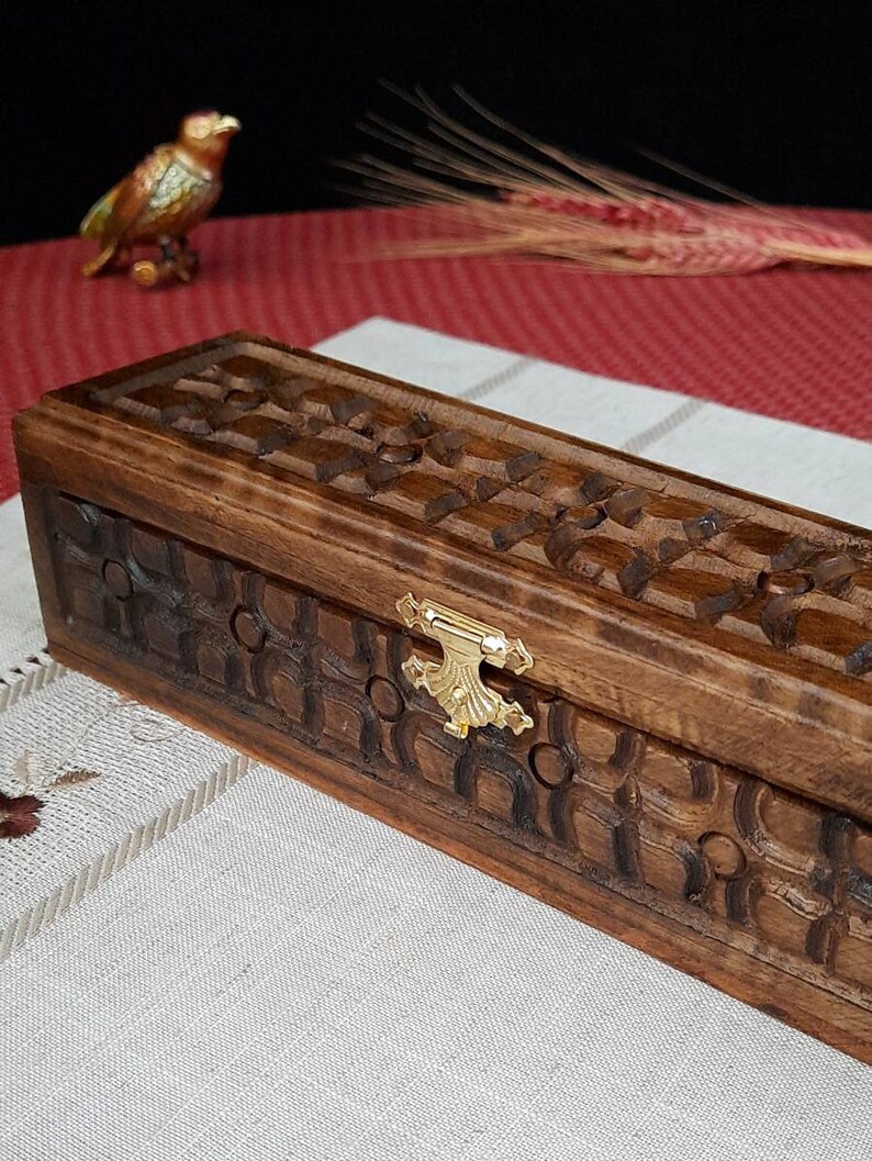 May include: A rectangular wooden box with a carved design and a gold metal latch. The box is made of dark wood and has a natural finish.