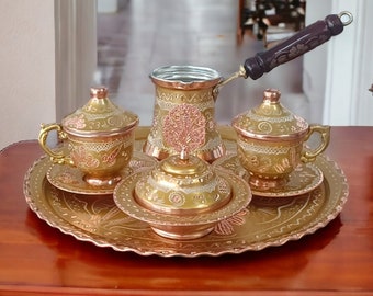 May include: A traditional Turkish coffee set with a copper pot, two cups, a sugar bowl, and a tray. The set is decorated with intricate floral patterns and has a gold finish.