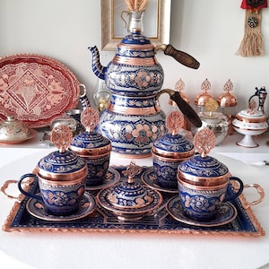 May include: A set of blue and copper Turkish teacups and saucers with intricate floral designs. The set includes a matching teapot with a traditional design.