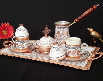 May include: A white and copper Turkish coffee set with floral designs on a copper tray. The set includes a coffee pot, two cups, a sugar bowl, and a small lidded container.