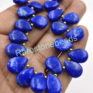 May include: A strand of deep blue lapis lazuli gemstone beads in a teardrop shape. The beads are strung on a gold wire with gold spacers between each bead. The beads have a natural, slightly rough texture.