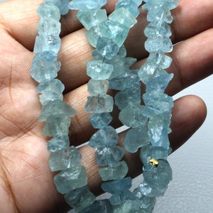 May include: A strand of light blue aquamarine gemstone beads. The beads are irregular in shape and have a rough, natural finish.