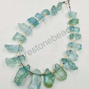 May include: A strand of light blue aquamarine gemstone beads, each bead is a rough, irregular shape. The beads are strung on a gold wire with gold spacers between each bead.