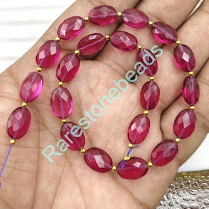 Puede incluir: Una hebra de cuentas de piedras preciosas rosadas talladas en forma ovalada con separadores dorados. Las cuentas están enhebradas en un cordón azul fino.