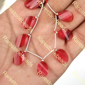 May include: A strand of red gemstone beads on a silver chain. The beads are oval shaped and have a translucent appearance.